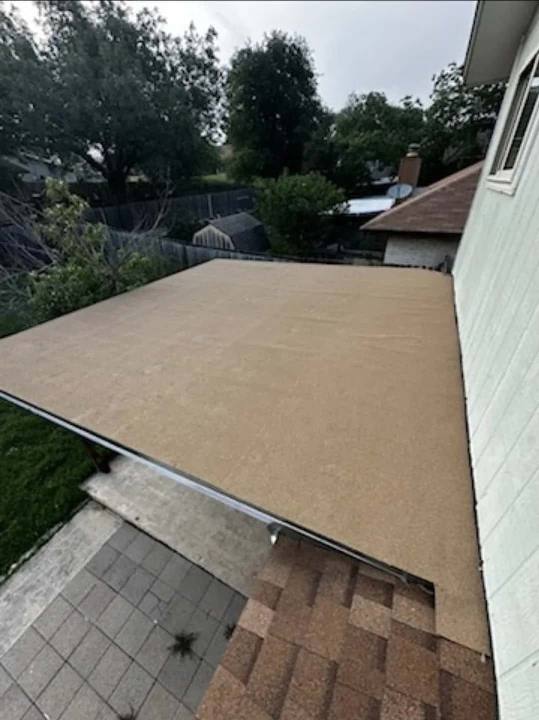 Tan granulated cap sheet on a low-slope roof section beside a shingle slope, backyard beyond
