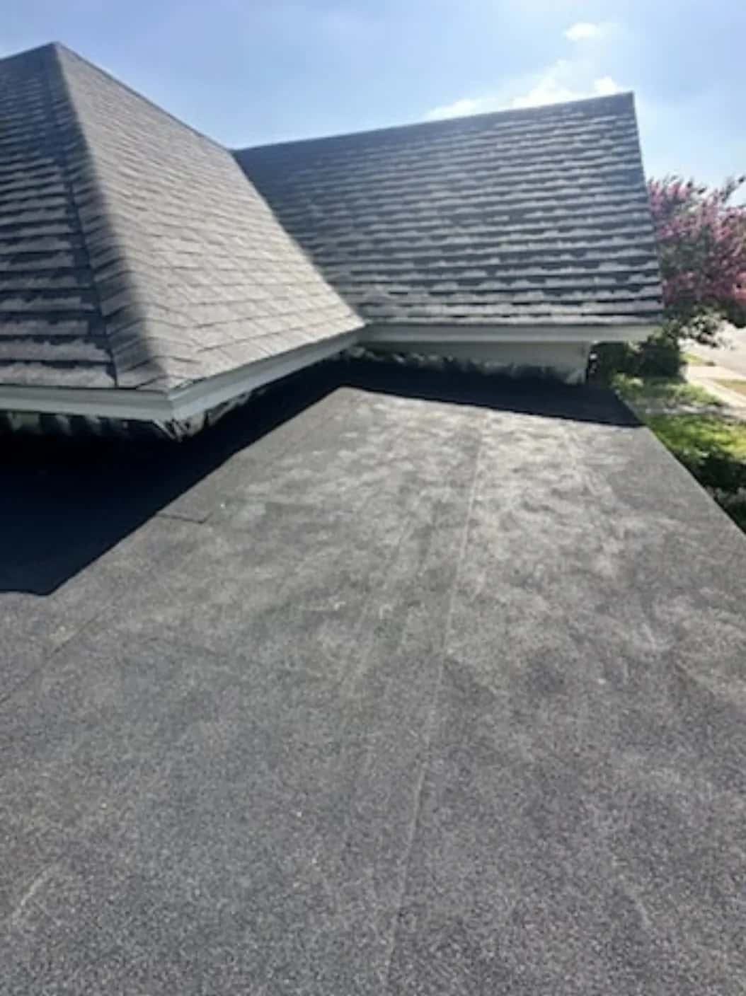 Low-slope modified bitumen roof section between two gray shingle gables