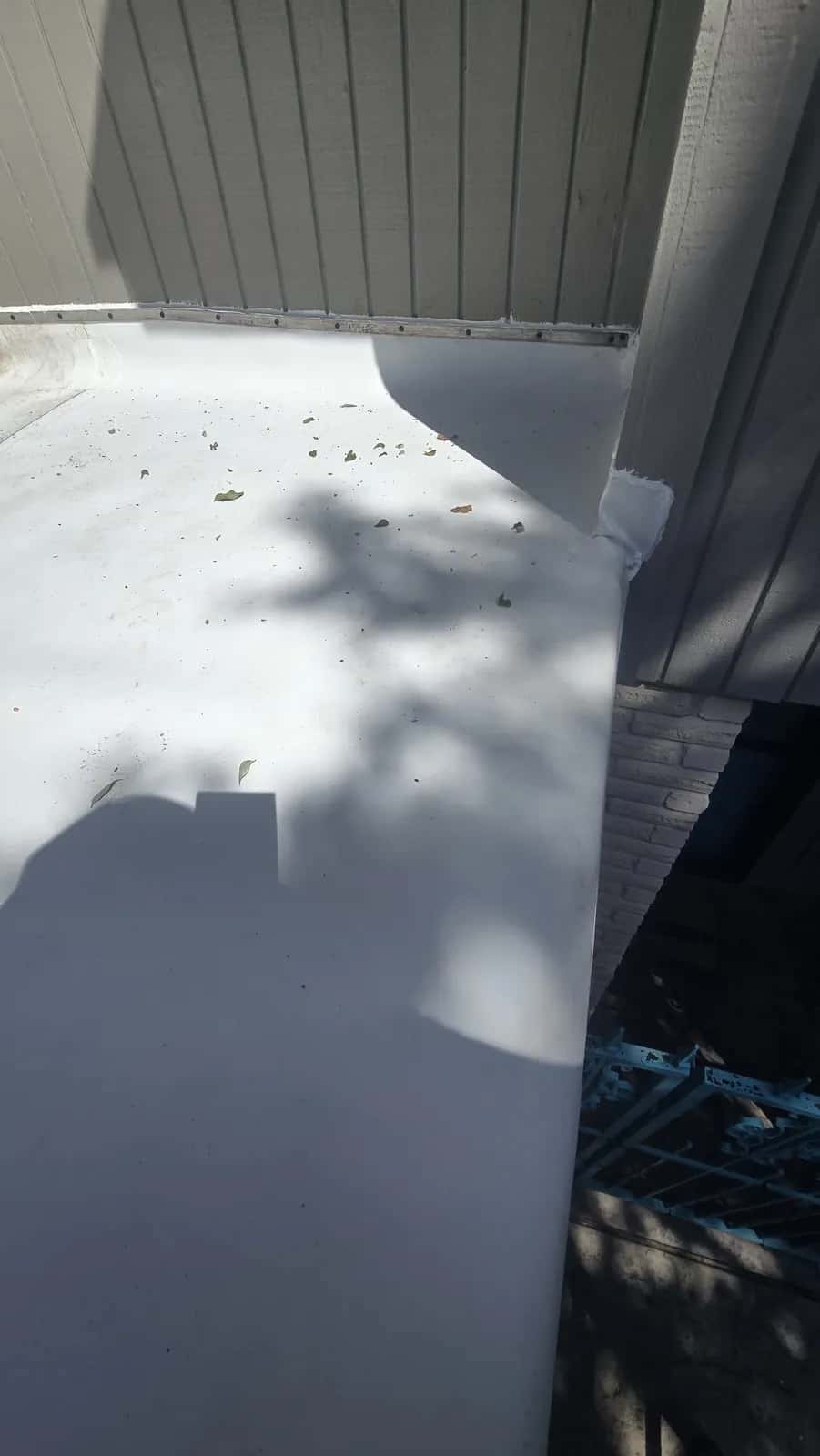 White TPO membrane flat roof section meeting a gray lap-sided wall with new flashing at the transition