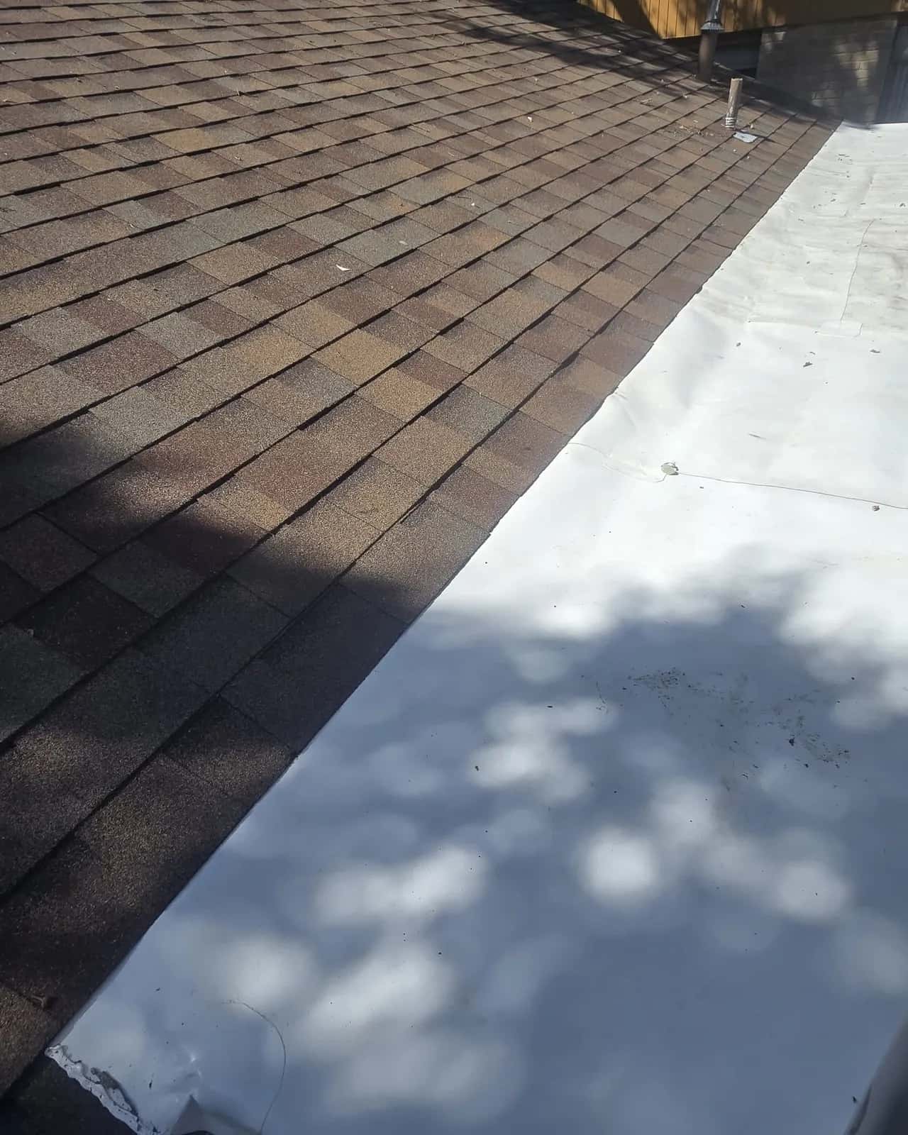 Brown architectural shingle slope meeting a white TPO membrane low-slope section with a wall at the top