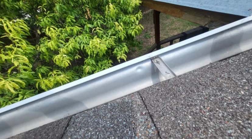 Close-up of a new gutter and drip edge along a shingle roof eave with trees beyond