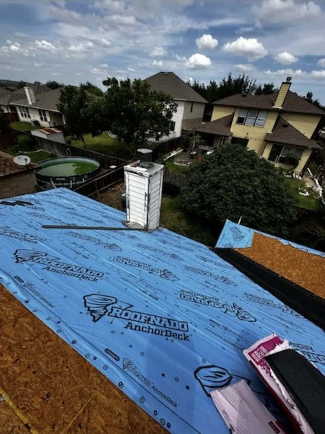Blue synthetic underlayment over new decking with a sided chimney, backyard pool below.