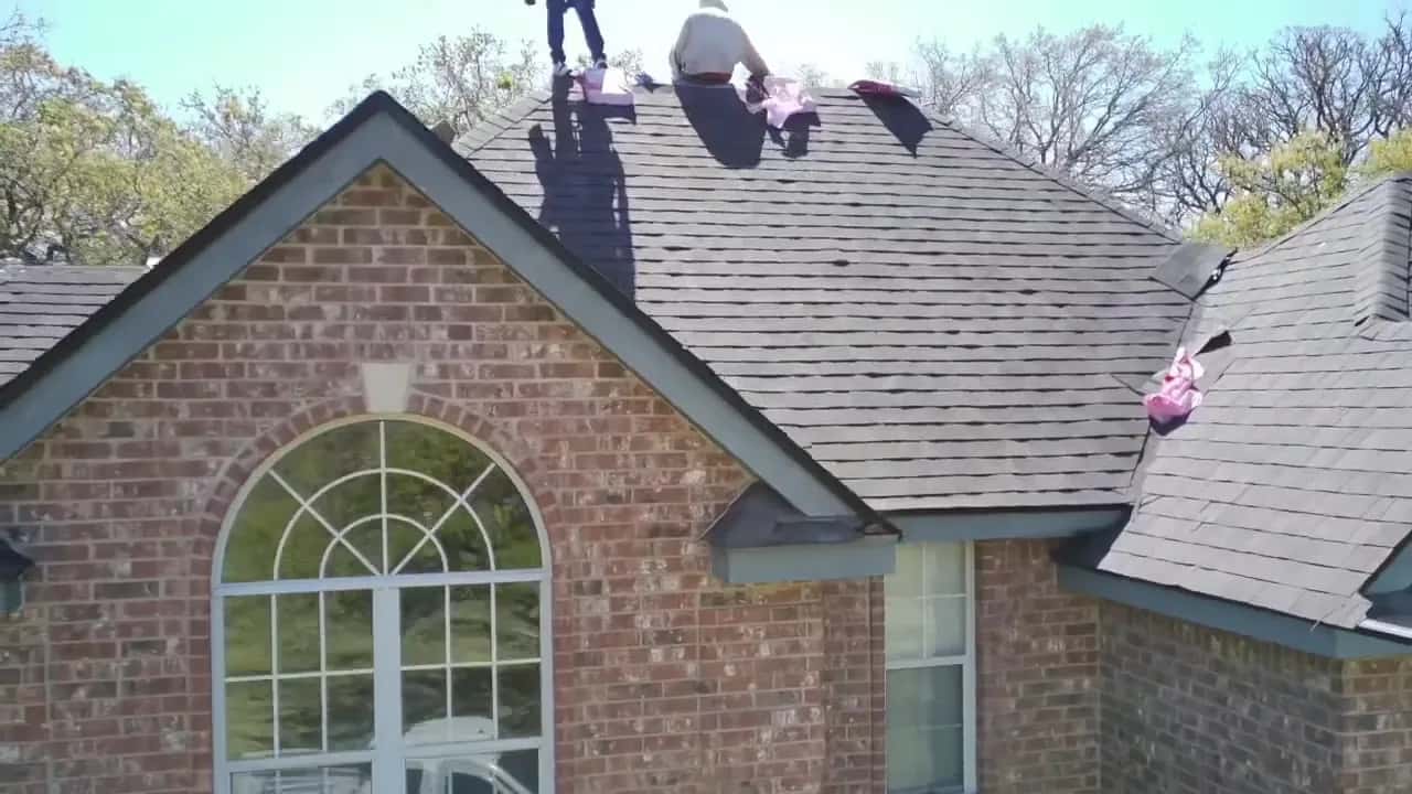 Crew installing gray architectural shingles on a brick home with an arched front window.