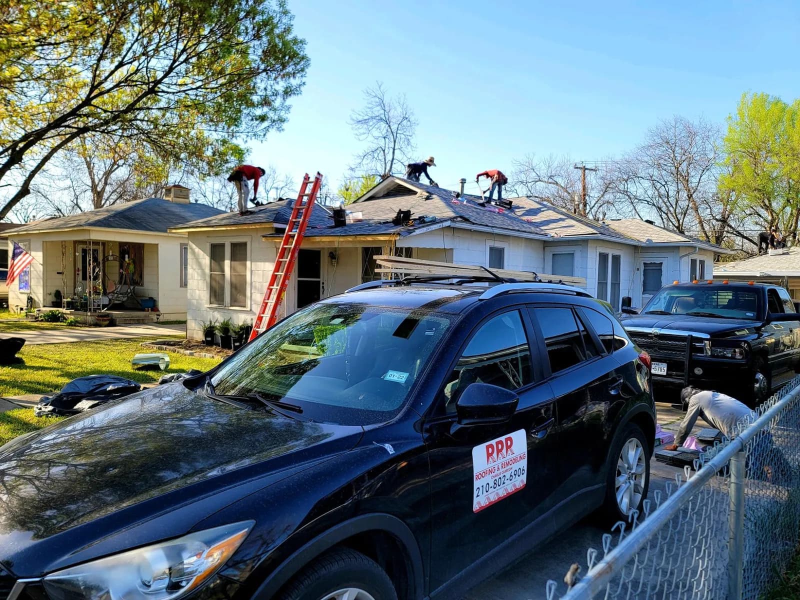 Roofing crews on two neighboring single-story homes with a company car and work truck parked out front.