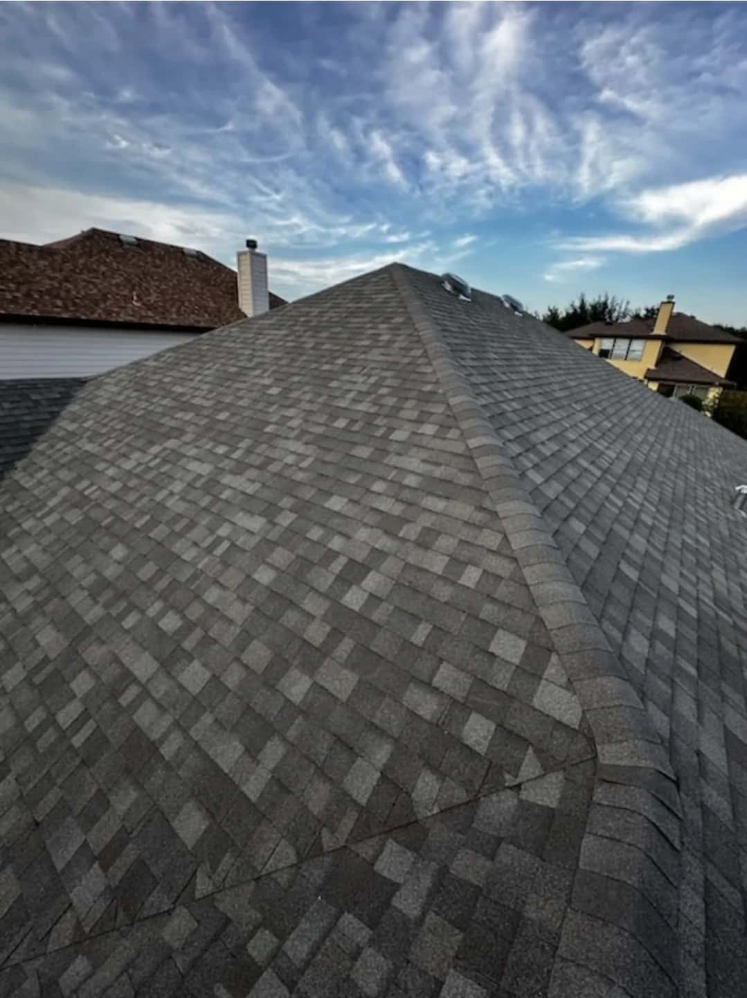 New gray architectural shingle hip ridge under a dramatic cloud-streaked sky