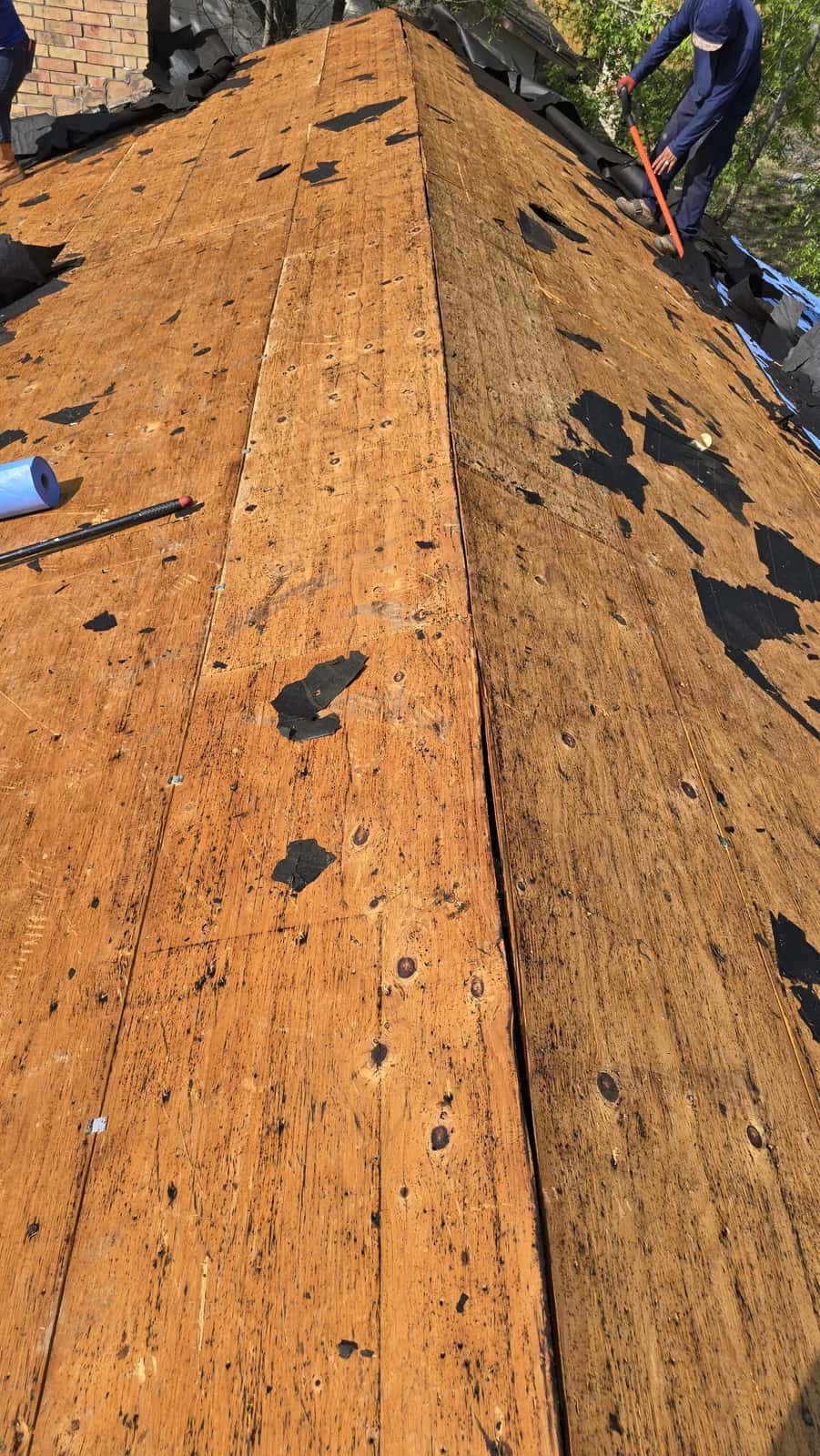 New plywood roof decking at the ridge of a home with a roofer at the far end, ready for underlayment