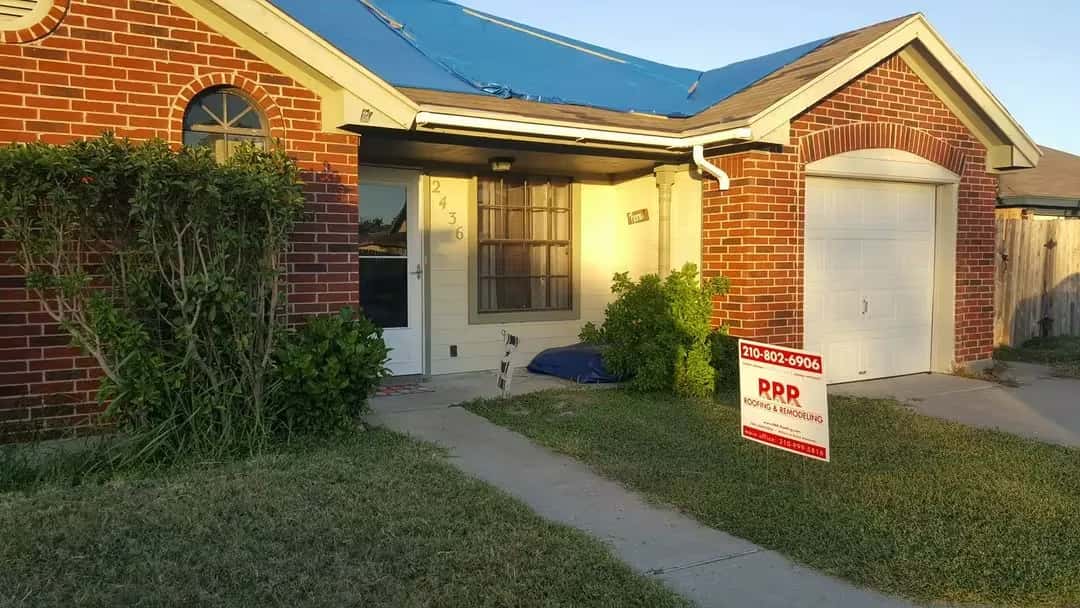 Red brick home with blue underlayment on the roof during a replacement and an RRR Roofing sign in the front yard.