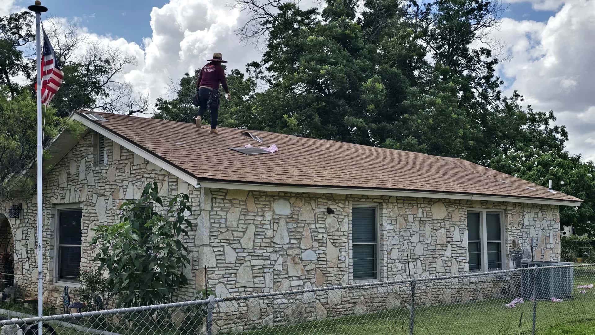 Limestone rock home with a newly installed brown architectural shingle roof, roofer finishing the ridge