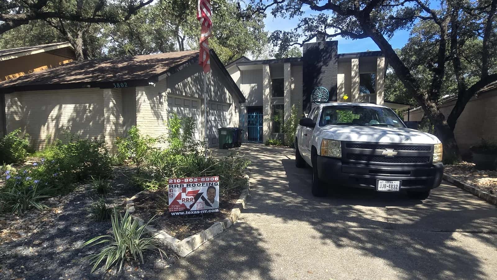Single-story stone home with a brown shingle roof, white work pickup in the driveway and an RRR Roofing yard sign in the landscaping.