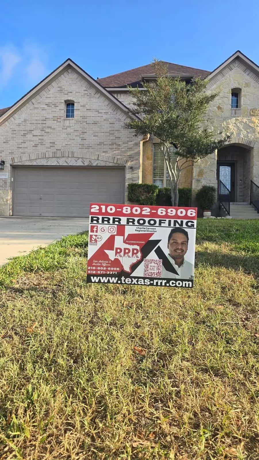 RRR Roofing yard sign with Charlie Carreon, owner, on the lawn of a stone and brick two-story home after its new roof.