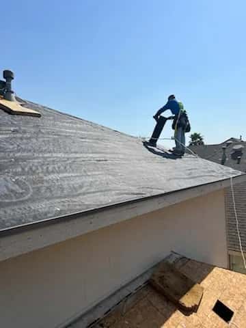 Roofer at the eave of a roof covered in synthetic underlayment with a dormer behind