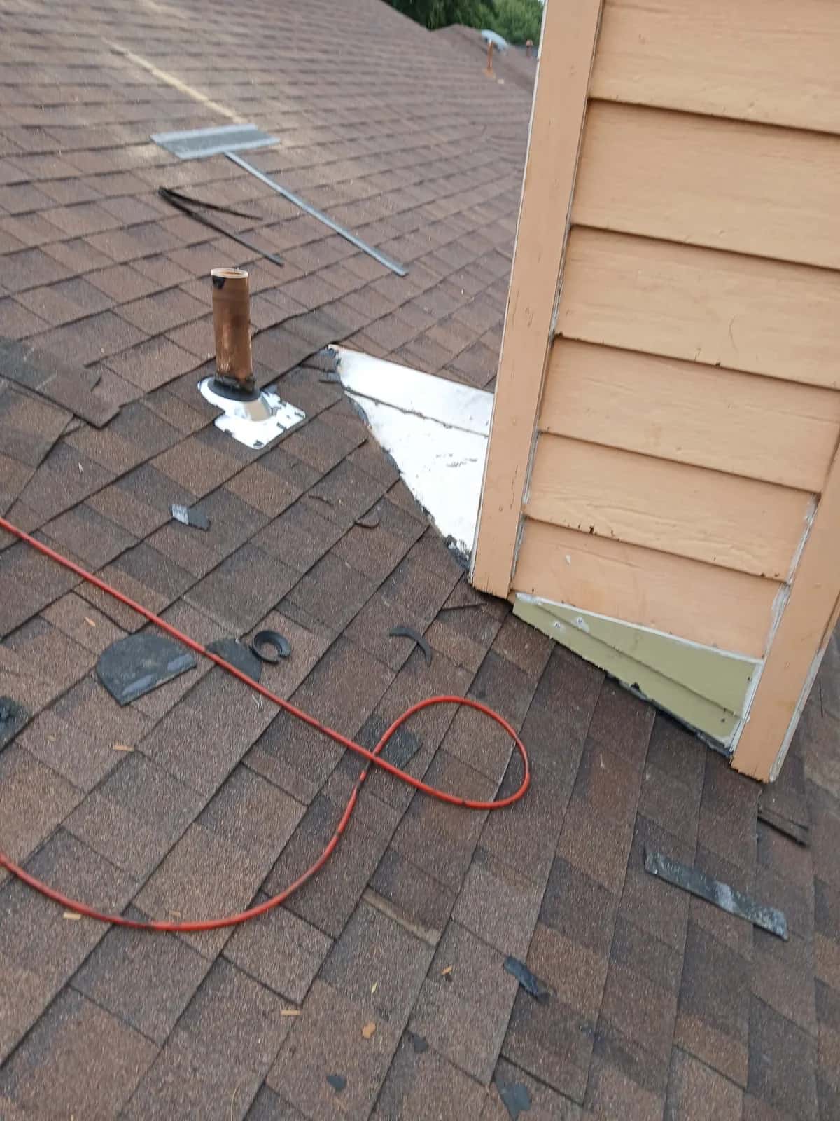 Brown shingle roof at a sided wall with a pipe boot and the step flashing area prepped for repair
