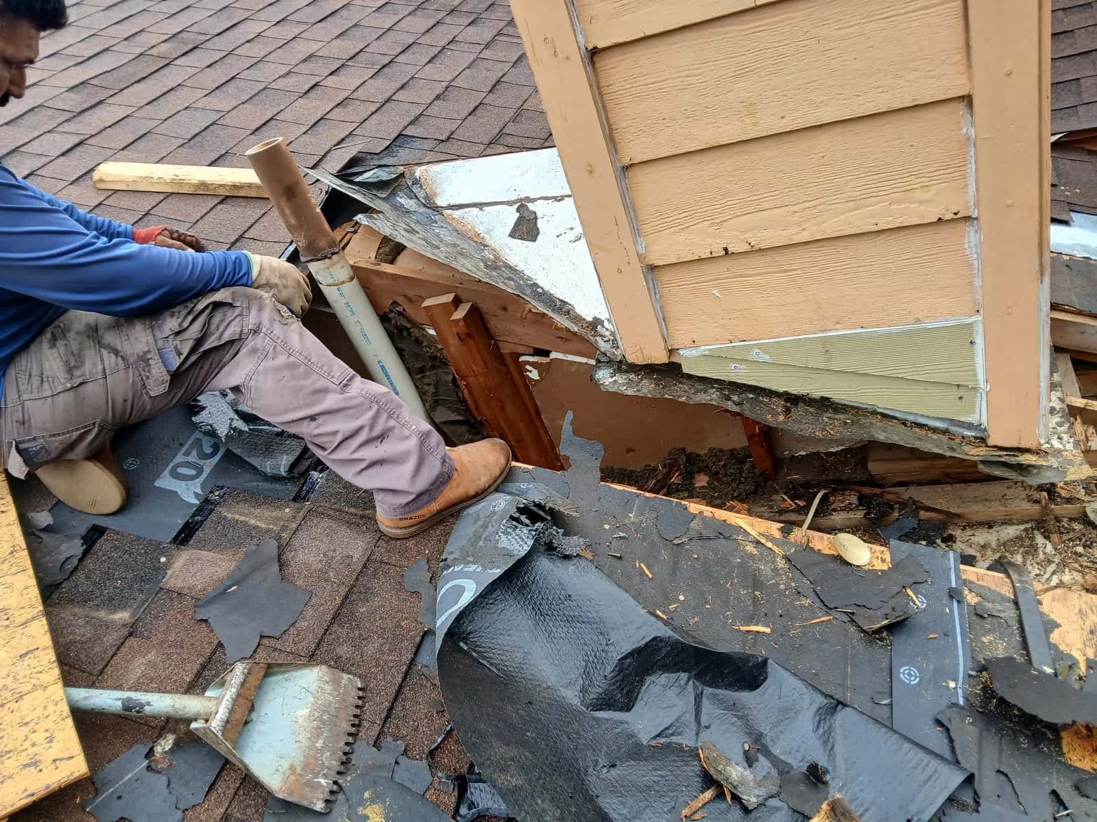 Roofer removing rotted trim and roofing at a wall junction during a roof repair