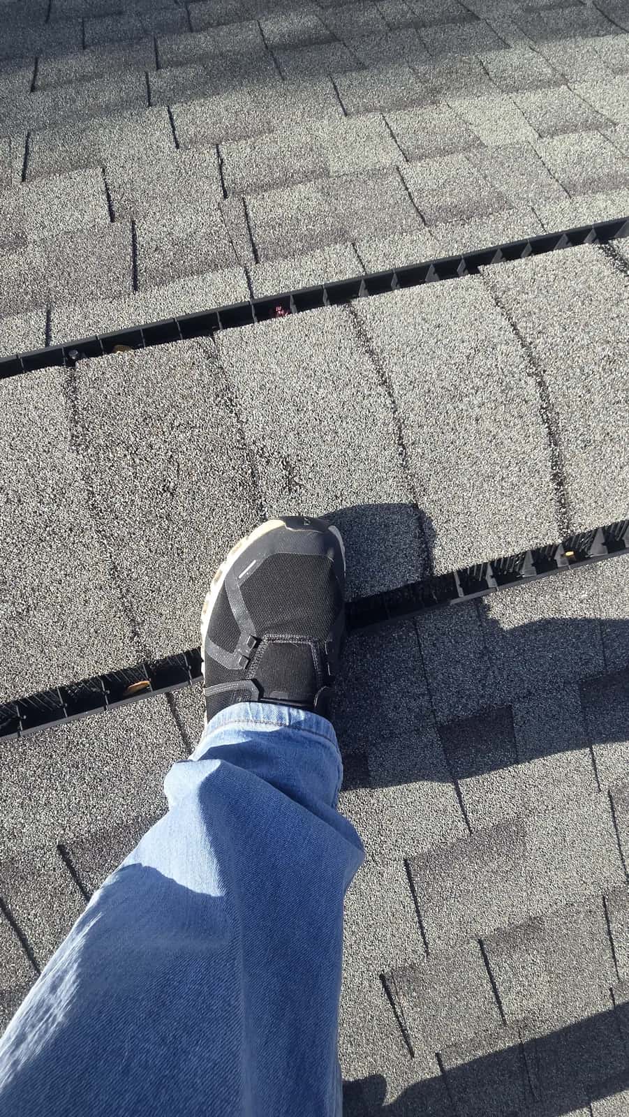 Chalk circle marking a hail hit on a gray asphalt shingle roof with an inspector's shoe beside it.