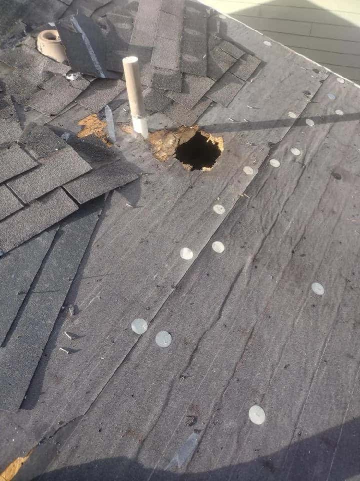 Damaged roof with a hole through the decking, torn felt and missing shingles, the kind of opening that lets water into a home