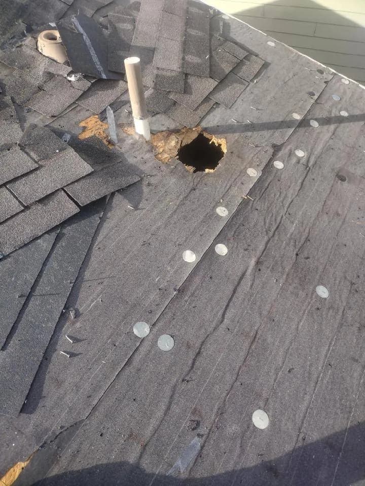 Damaged roof with a hole through the decking, torn felt and missing shingles before repair.