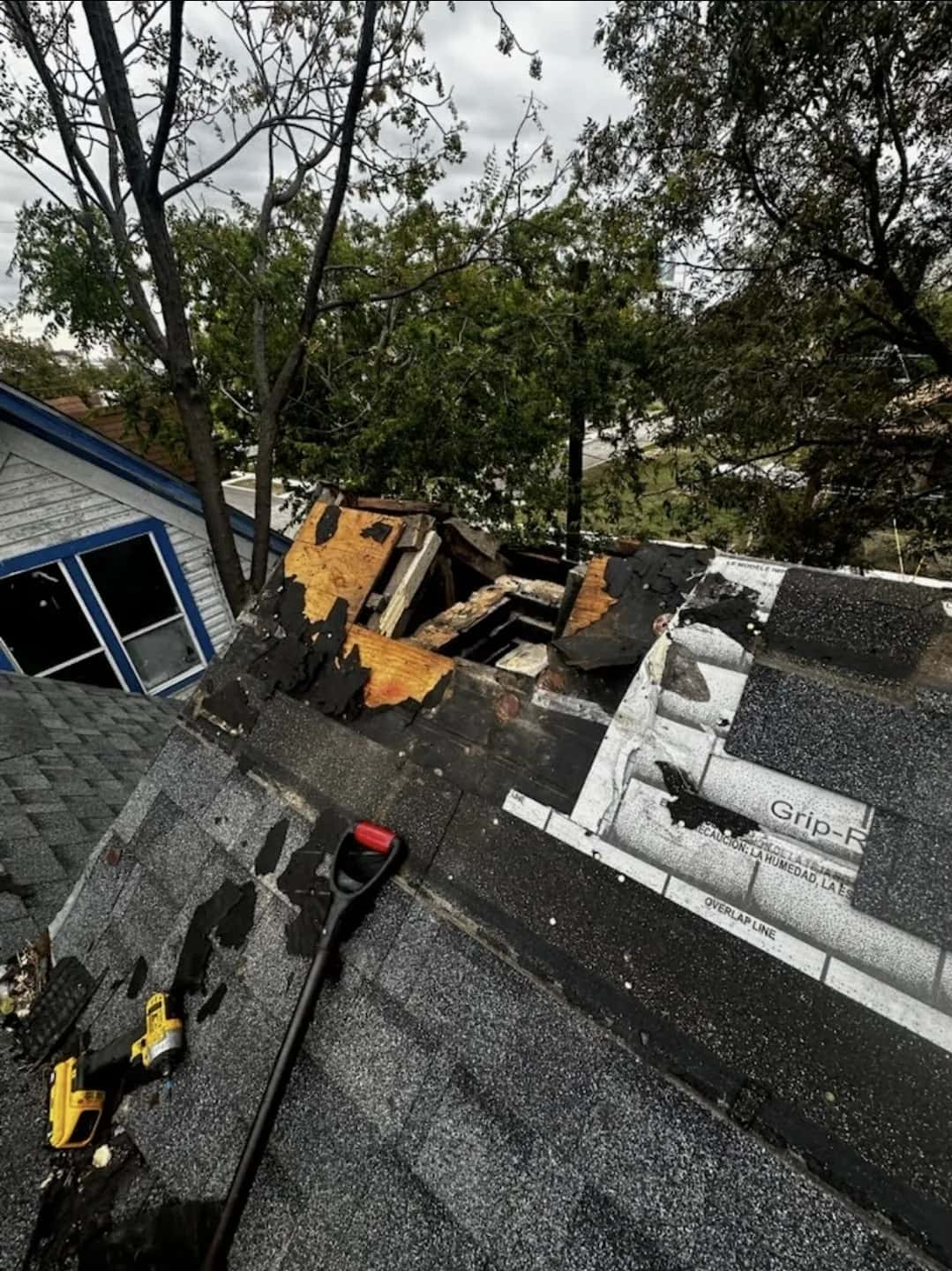 Tear-off revealing rotted, moisture-damaged roof decking and deteriorated felt beneath old shingles, tools on the roof