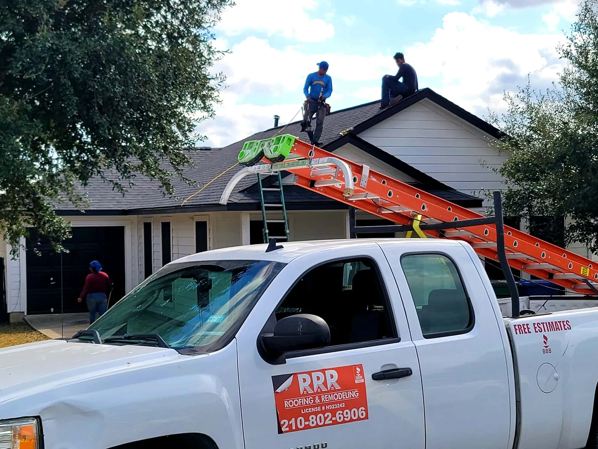 White Texas-RRR company pickup with an RRR door magnet and ladder rack parked at a home with two crew members on the roof
